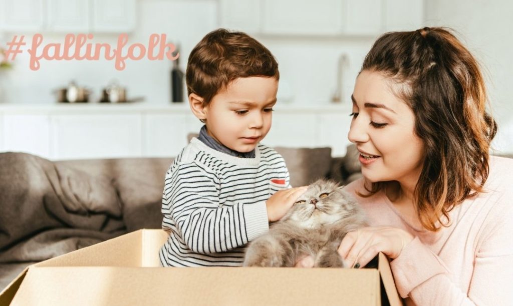 Towarzyski charakter. Dziecko z mamą patrzy na małego kotka w kartonie. Napis fallinfolk po lewej stronie.
