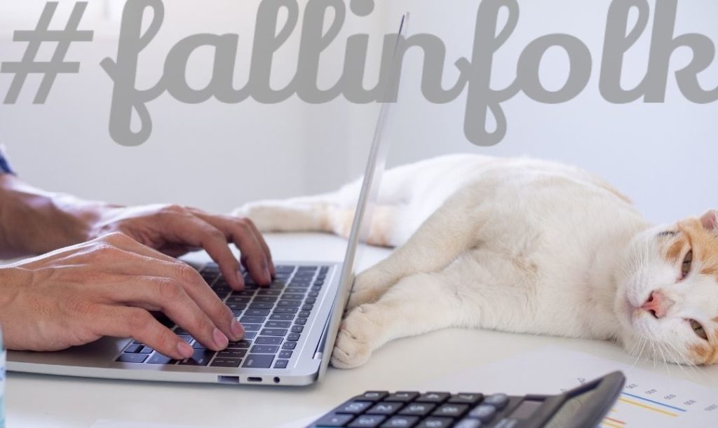 Przebywanie blisko Ciebie. Biały kot lezy przy laptopie piszącego na klawiaturze człowieka. Napis fallinfolk.