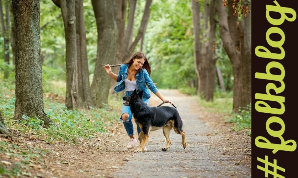 Zdrowie i dobra kondycja. Zdjęcie bawiącej się z psem kobiety na spacerze. Napis folkblog. 
