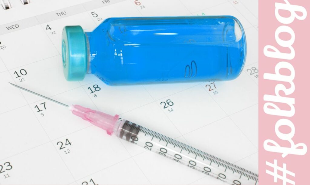 Kalendarz szczepień. Zdjęcie leżącej na kalendarzu ampułki i strzykawki. Napis folkblog.