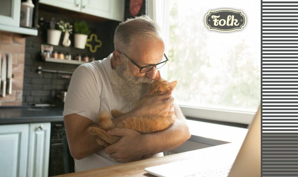 może żyć naprawdę długo. Zdjęcie starszego mężczyzny całującego rudego kota, którego trzyma na rękach. Po prawej stronie element graficzny w paski i szare logo FOLK.