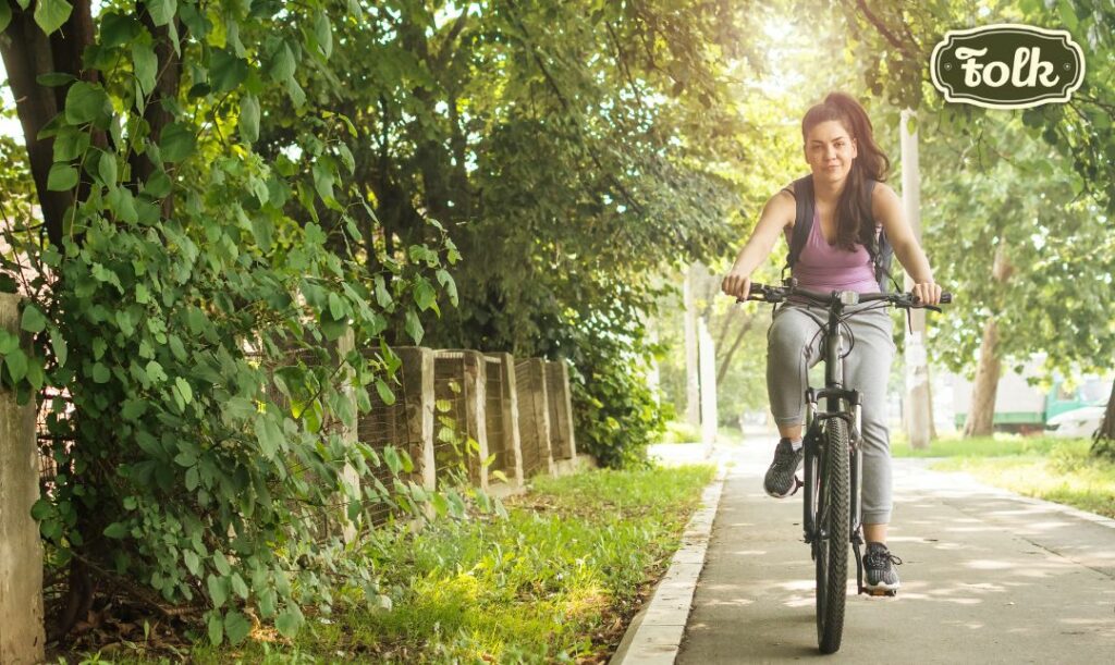 Jazda rowerem. Zdjęcie kobiety na rowerze wśród zieleni ulicznej. Logo FOLK na zielonym tle. 